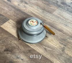 Vintage metal musical powder box with butterscotch bakelite handle and porcelain medallion lid